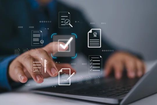 Mão tocando tela digital com ícones de documentos verificados e checklist sobre notebook, conceito de regularização documental online, tons azul e cinza com destaque laranja, fotografia tecnológica realista
